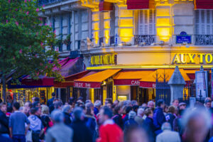Une rue animée le soir, grouillante de monde, dévoilant une vue sur un café parisien.